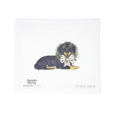 Hand-painted 18 mesh needlepoint canvas featuring a highly detailed black dachshund wearing a festive Christmas bow and holly around its neck. Designed as a beautiful ornament, perfect for holiday decorating, gifting, or commemorating a beloved pet.