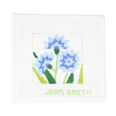 Hand-painted needlepoint canvas featuring a stylized Bachelor's Button flowers in shades of blue on white mesh, designed by Jean Smith—perfect for finishing as a garden-themed ornament, framed decor, or a fun coaster