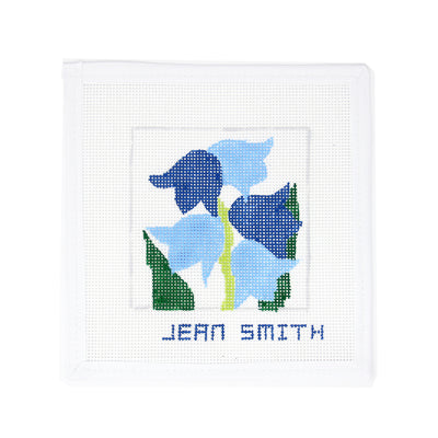 Hand-painted needlepoint canvas featuring a stylized Delphinium flower in shades of blue on white mesh, designed by Jean Smith—perfect for finishing as a garden-themed ornament, framed decor, or a fun coaster